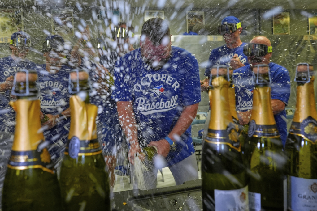 Toronto Blue Jays manager John Schneider, center, celebrates with players in the clubhouse after their a baseball game against the Kansas City Royals, Sunday, Sept. 21, 2025, in Kansas City, Mo. (AP Photo/Charlie Riedel)