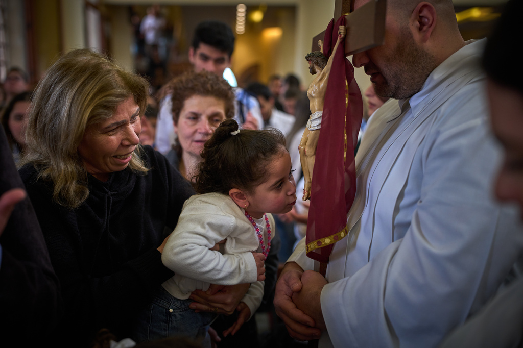 A girl kisses a cross held by a priest during Good Friday Mass at St. Anthony Church, which was devoted to expressing solidarity with Christian villagers in southern Lebanon displaced by the war in Jdeideh, a suburb of Beirut, Lebanon, Friday, April 3, 2026. (AP Photo/Emilio Morenatti)