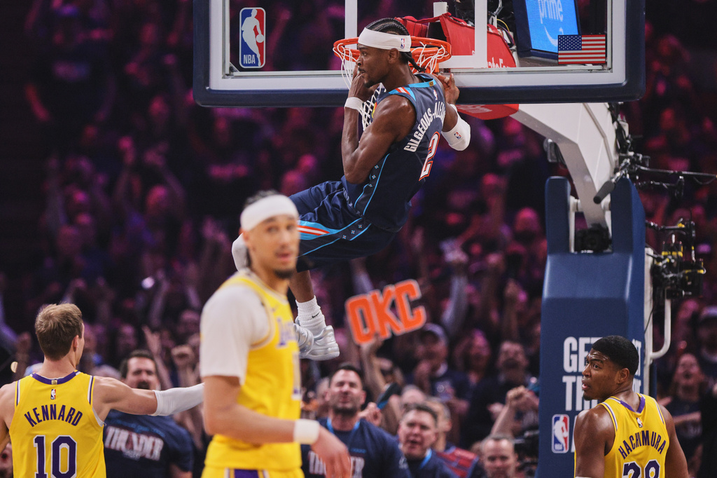 Oklahoma City Thunder guard Shai Gilgeous-Alexander hangs on the rim after dunking as Los Angeles Lakers' Luke Kennard (10), Jaxson Hayes, front, and Rui Hachimura (28) react to the play in the first half of Game 2 in a second-round NBA basketball playoffs series Thursday, May 7, 2026, in Oklahoma City. (AP Photo/Nate Billings)