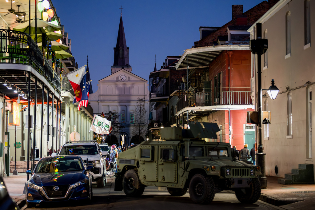 A man walking on Bourbon Street holds a flag reading "Love" as an armored vehicle sits parked on a street in the French Quarter as part of a National Guard deployment for New Year's celebrations in New Orleans, Tuesday, Dec. 30, 2025. (AP Photo/Matthew Hinton)