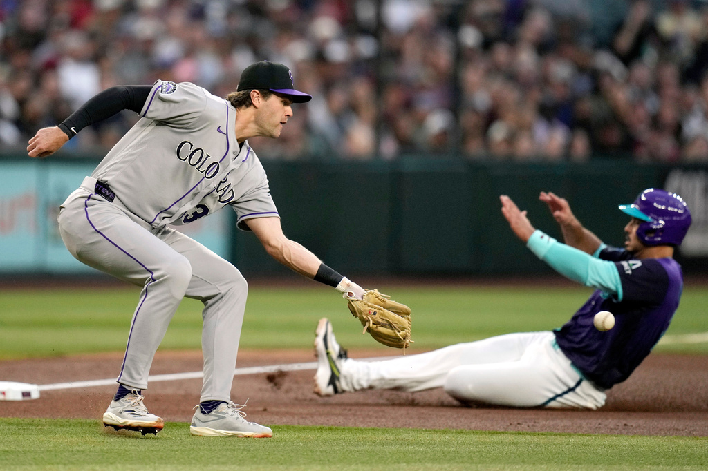 Colorado Rockies third baseman Chad Stevens, left, reaches out to catch a late throw as Arizona Diamondbacks' Nolan Arenado advances to third base during the second inning of a baseball game, Friday, May 22, 2026, in Phoenix. (AP Photo/Ross D. Franklin)