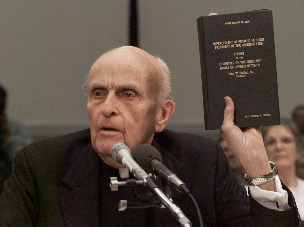 FILE - Former Massachusetts Rep. Father Robert Drinan holds a copy of the 1974 impeachment report of President Nixon while testifying before the House Judiciary Committee's impeachment hearing on Capitol Hill in Washington, on Dec. 8, 1998. (AP Photo/J. Scott Applewhite, File)