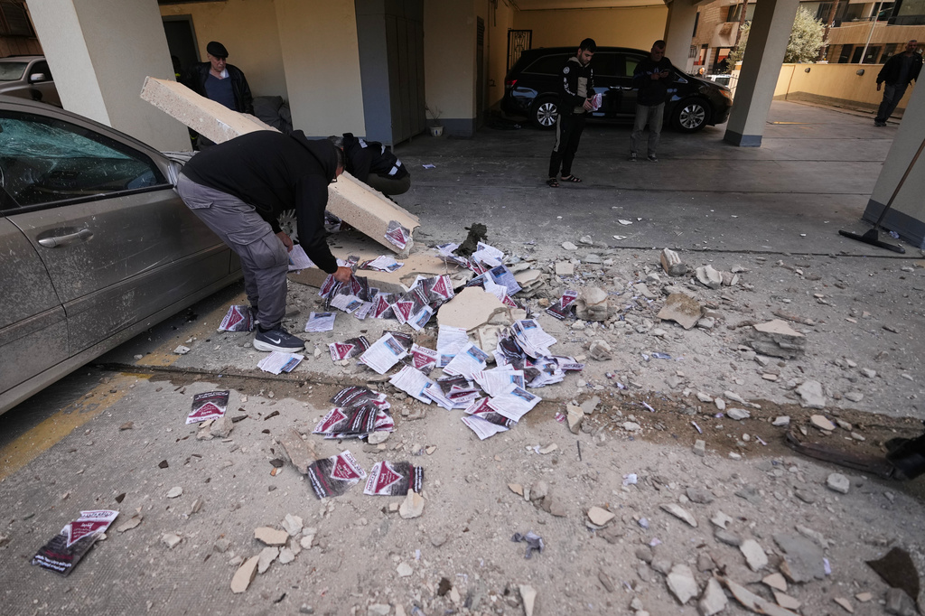 People collect leaflets scattered on the ground at a site where a projectile carrying them hit an apartment building in Beirut, Lebanon, Saturday, March 28, 2026. (AP Photo/Hassan Ammar)