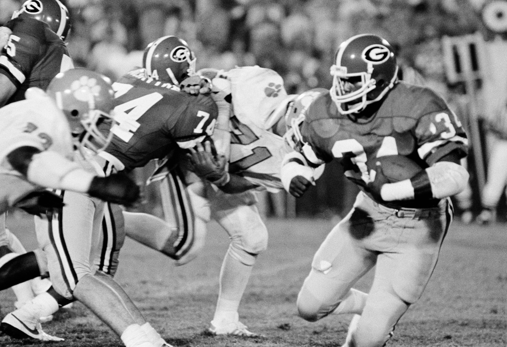 FILE - Georgia's Herschel Walker (34) goes around Clemson's Dan Benish (71) with some help from Georgia's Guy McIntyre (74) during third period of an NCAA college football game Monday night, Sept. 6, 1982 in Athens, Ga. (AP Photo/Charles Kelly, File)