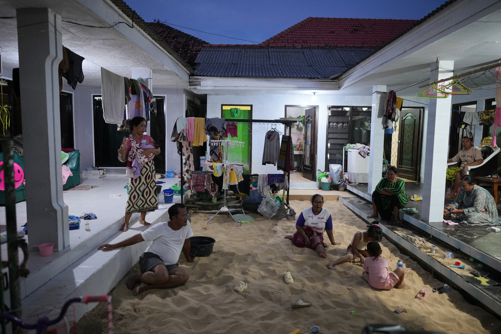 Marsadik, lower left, one name only, sits in a sandpit with his family members at home in Legung Timur village in Sumenep on Madura Island, Indonesia, Tuesday, Sept. 9, 2025. (AP Photo/Dita Alangkara)