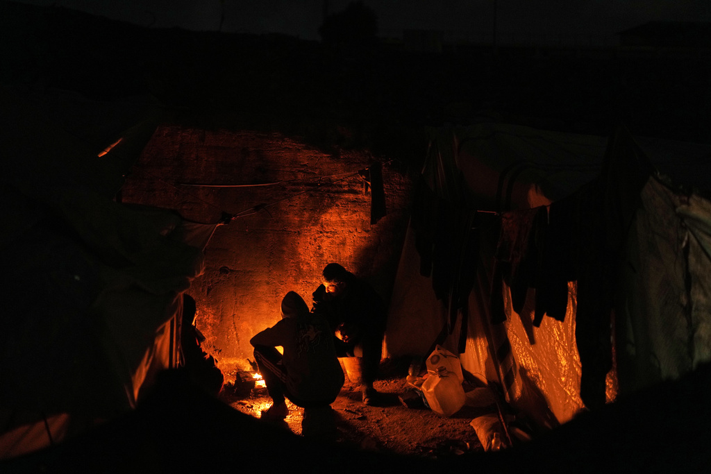 Displaced Palestinians cook and warm themselves around a fire at a tent camp in Gaza City, Sunday, Jan. 18, 2026. (AP Photo/Jehad Alshrafi)