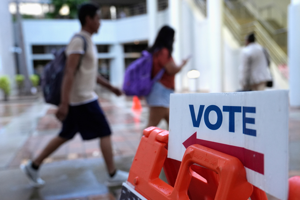FILE - People walk past a "vote" sign on the first day of early voting in the general election in Miami, Oct. 21, 2024. (AP Photo/Lynne Sladky, File)