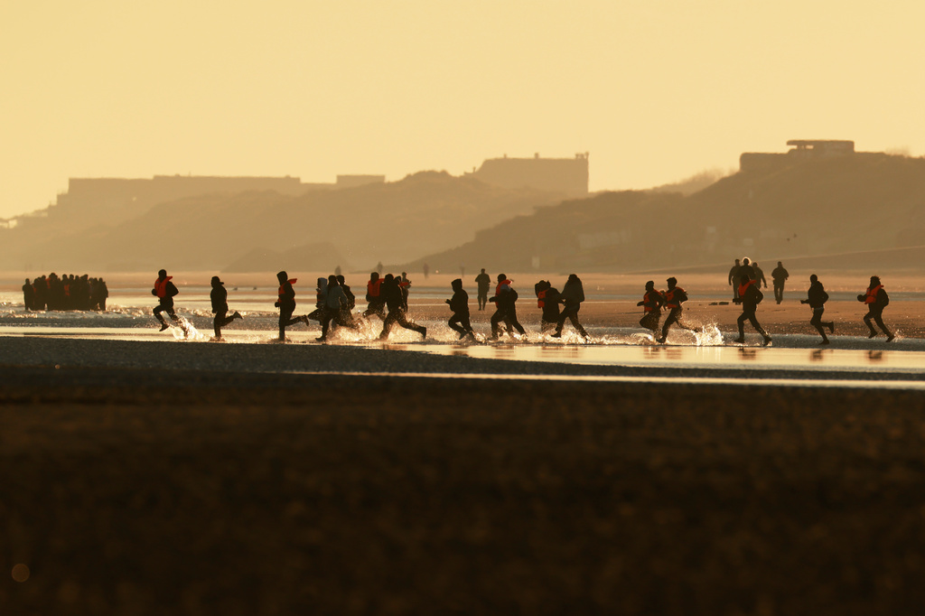 Migrants run to board a small boat in an attempt to reach Britain, Wednesday, April 8, 2026 in Malo-les-Bains, northern France. (AP Photo/Jean-Francois Badias)