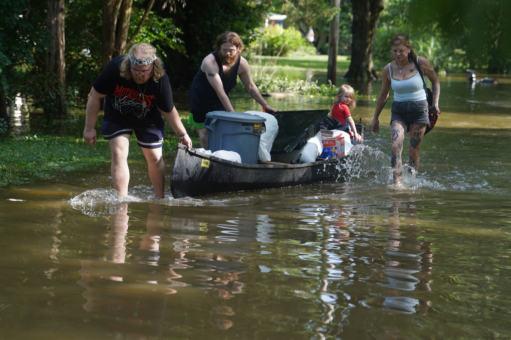 Scott Conrad, left, Joseph Workman, second from left, Ronan Carey, in the boat, and Kesley Patterson use a kayak to transport items from their flooded homes in Indianapolis, Sunday, Aug. 16, 2026. (AP Photo/Obed Lamy)