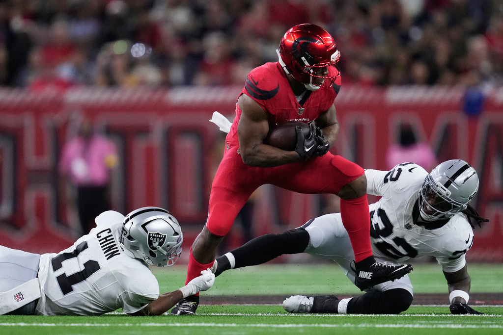 Houston Texans running back Nick Chubb, middle, runs against Las Vegas Raiders safety Jeremy Chinn (11) and safety Lonnie Johnson Jr. during the second half of an NFL football game, Sunday, Dec. 21, 2025, in Houston. (AP Photo/Ashley Landis)