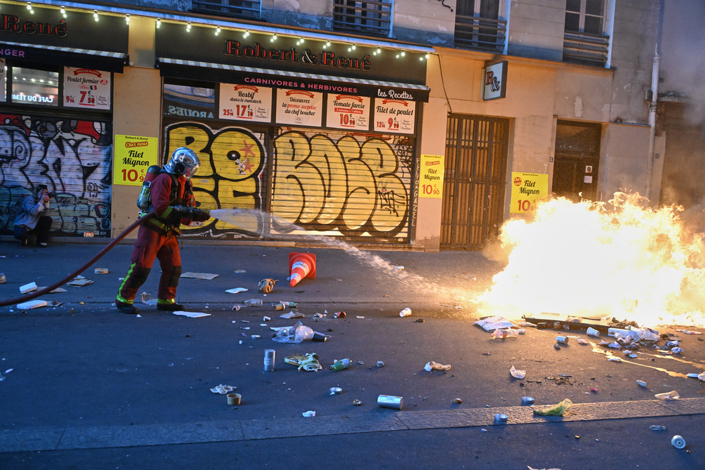 A firefighter extinguishes a fire during clashes with police a day after a demonstration against rising living costs, joining students' grievances, in Paris, Sunday, Oct. 18, 2026. (AP Photo/Emma Da Silva)