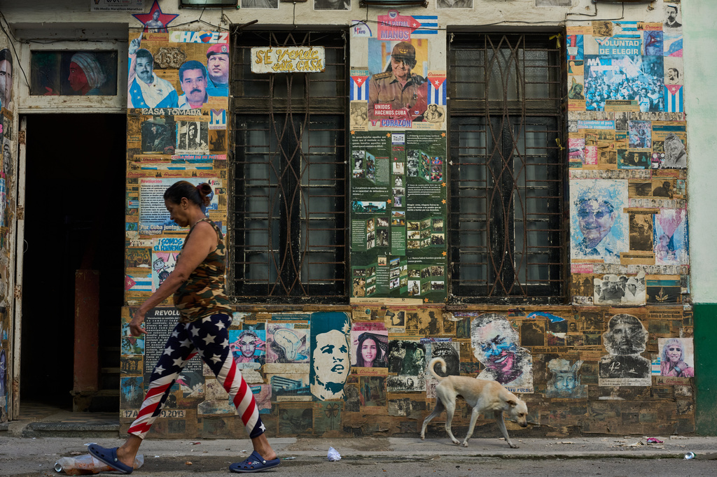 A woman wearing U.S. flag motif pants walks past a building that houses an art installation on the Cuban Revolution, featuring photos of former Cuban President Raul Castro and former Venezuelan President Nicolas Maduro, in Havana, Cuba, Tuesday, May 19, 2026. (AP Photo/Ramon Espinosa)