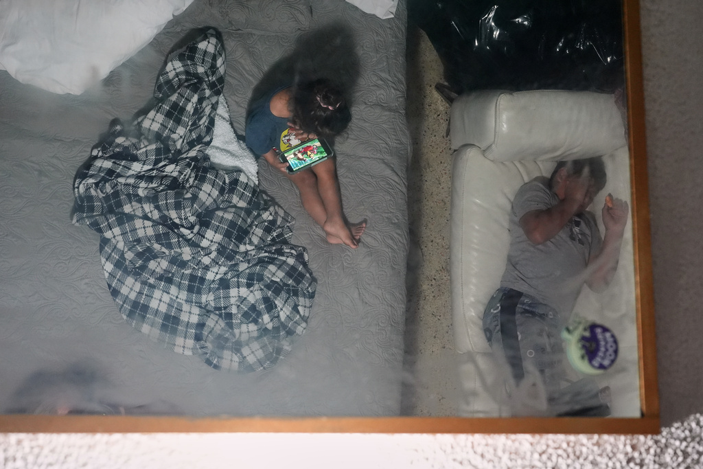 Two brothers are reflected in a ceiling mirror as they pass the time in the Miami-area motel room where they are living with their pregnant mother Yaoska after their father was deported to Nicaragua, Thursday, Nov. 13, 2025. (AP Photo/Rebecca Blackwell)