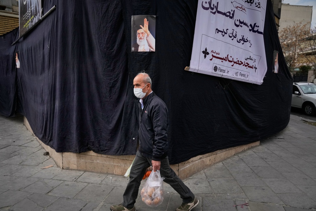 AA man carrying groceries walks by a picture of the late Iranian Supreme Leader Ayatollah Ali Khamenei hanging on a black sheet along the side of a mosque in Tehran, Iran, Monday, March 2, 2026. (AP Photo/Vahid Salemi)