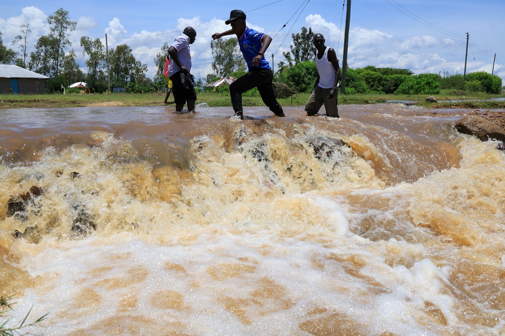 People cross a flooded portion of the road following heavy rains in Nyakach, Western Kenya, Tuesday, March 24, 2026. (AP Photo/Andrew Kasuku)