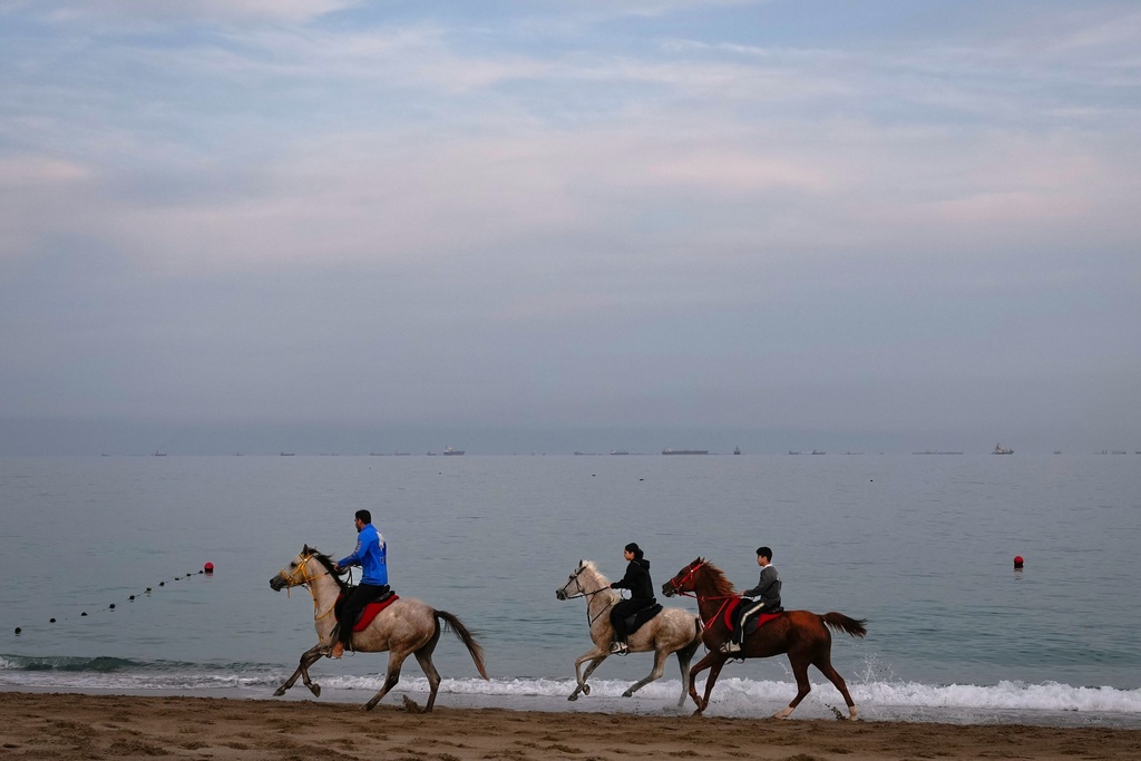 Riders gallop along a beach as oil tankers and cargo ships line up in the Strait of Hormuz near Khor Fakkan, United Arab Emirates, Wednesday, March 11, 2026. (AP Photo/Altaf Qadri)