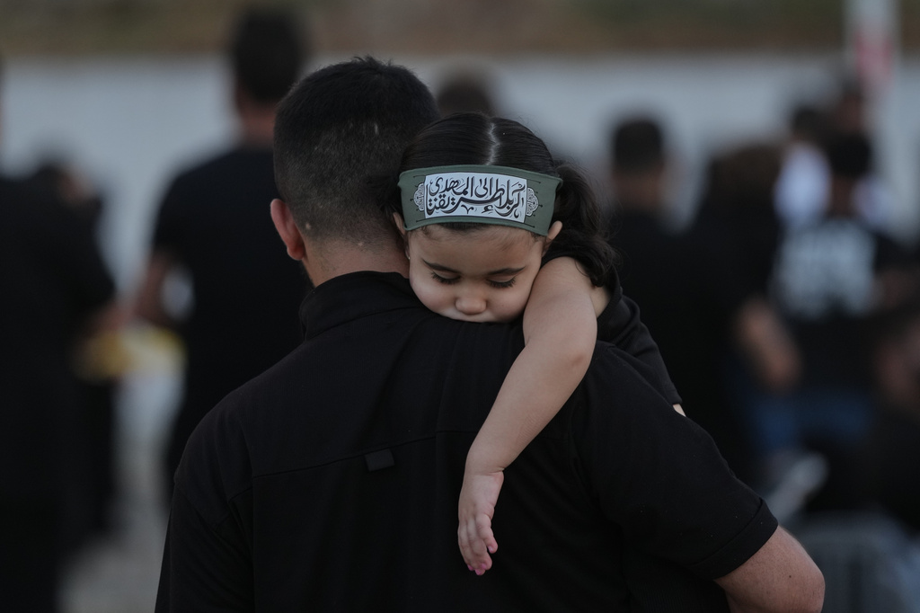 A girl wearing an Ashoura headband rests on her father's shoulder during a sermon marking the third day of Ashoura, the Shiite Muslim commemoration of the 7th-century death of Imam Hussein, the grandson of the Prophet Muhammad, in the southern port city of Tyre, Lebanon, Friday, June 19, 2026. (AP Photo/Hassan Ammar)