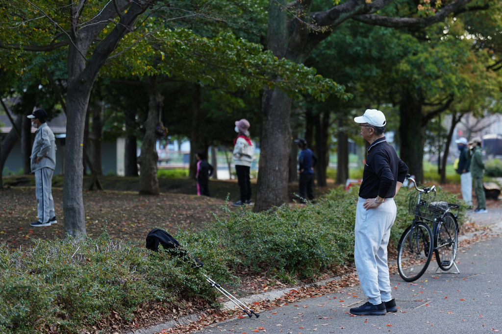 People perform a stretching exercise while listening to music and guidance from radio at a public park in Tokyo, Monday, April 6, 2026. (AP Photo/Hiro Komae)