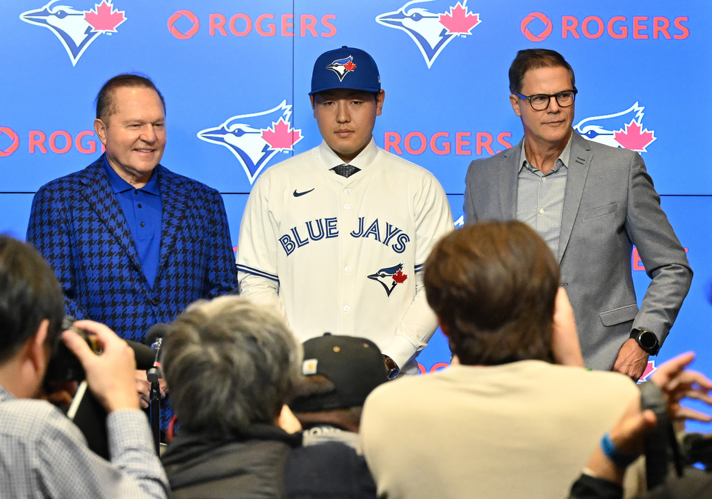 Kazuma Okamoto, center, the Toronto Blue Jays newest signing, dons a jersey at an introductory press conference with his attorney Scott Boras, left, and Blue Jays general manager Ross Atkins at Rogers Centre in Toronto, Canada, on Tuesday, Jan. 6, 2026. (Jon Blacker/The Canadian Press via AP)
