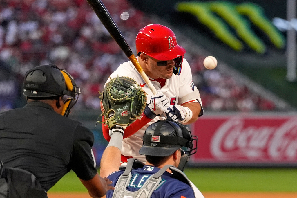 Los Angeles Angels' Mike Trout, center, is hit by a pitch as Seattle Mariners catcher Cal Raleigh, right, and home plate umpire Ramon De Jesus watch during the first inning of an opening-day baseball game Friday, April 3, 2026, in Anaheim, Calif. (AP Photo/Mark J. Terrill)