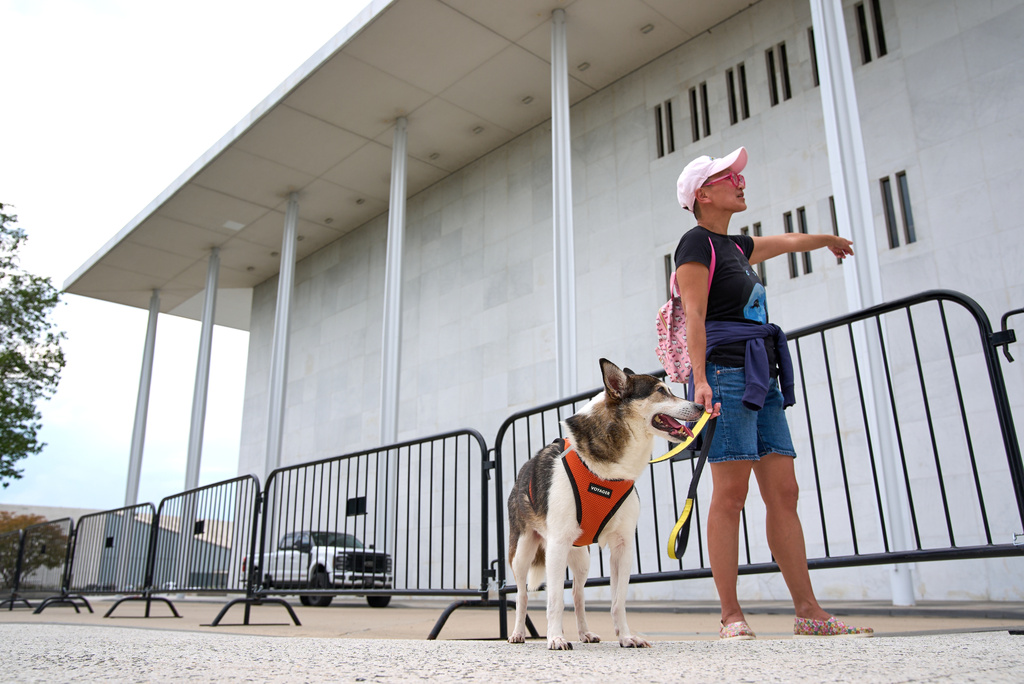 Quynh Pham of Washington, and her dog Jay, look at the Kennedy Center which has been fenced off and closed to the public, Thursday, Sept. 17, 2026, in Washington, "My husband and I moved to this neighborhood because we are big opera and ballet fans," says Pham, "we know the NSO players who live in the neighborhood, here you know exactly who is being affected." (AP Photo/Jacquelyn Martin)