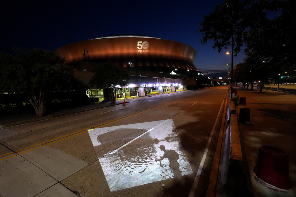 This photo of a man pushing his bicycle through floodwaters near the Superdome in the aftermath of Hurricane Katrina, taken by AP photographer Eric Gay, is projected Wednesday, Aug. 20, 2025, onto the same spot in New Orleans. (AP Photo/Gerald Herbert)