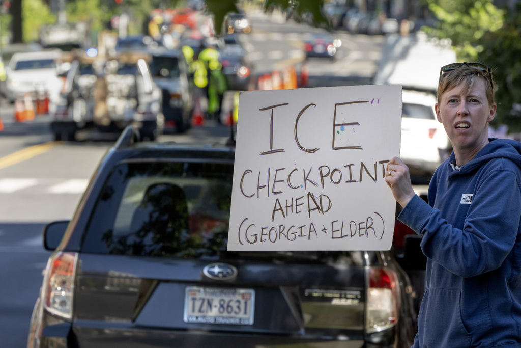 People hold signs warning drivers of a checkpoint operated by the Metropolitan Police Department and federal agencies, including officers from Immigration and Customs Enforcement (ICE) and Homeland Security Investigations (HSI), on Georgia Avenue in the northern part of Washington, Saturday, Aug. 30, 2025. (AP Photo/Mark Schiefelbein)