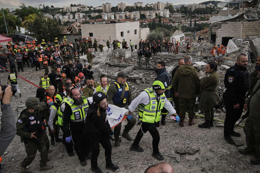 Rescue workers and military personnel carry a body of a victim from the scene where several people were killed by an Iranian missile strike in Beit Shemesh, Israel Sunday, March 1, 2026. (AP Photo/Leo Correa)