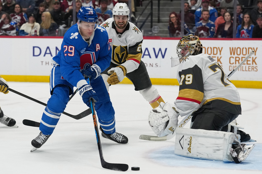 Colorado Avalanche center Nathan MacKinnon, left, puts a shot on Vegas Golden Knights goaltender Carter Hart, right, after driving past defenseman Shea Theodore in the third period of an NHL hockey game Saturday, April 11, 2026, in Denver. (AP Photo/David Zalubowski)