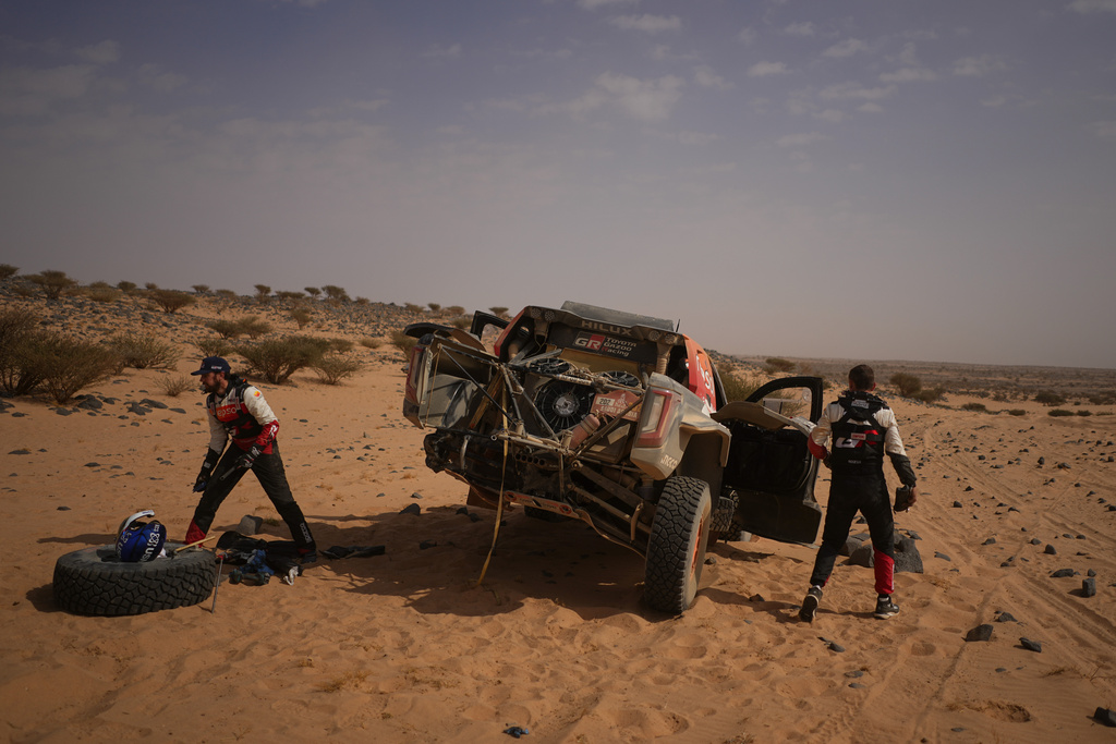 Driver Henk Lategan, left, and co-driver Brett Cummings repair their car during the eleventh stage of the Dakar Rally between Bisha and Al Henakiyah, Saudi Arabia, Thursday, Jan.15, 2026. (AP Photo/Thibault Camus)