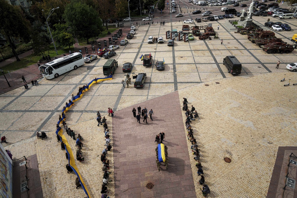 People kneel down, as honor guards carry the coffin of Artem Antonenko, a Ukrainian serviceman, during his funeral ceremony in the center of Kyiv, Ukraine, Friday, Sept. 19, 2025. (AP Photo/Evgeniy Maloletka)