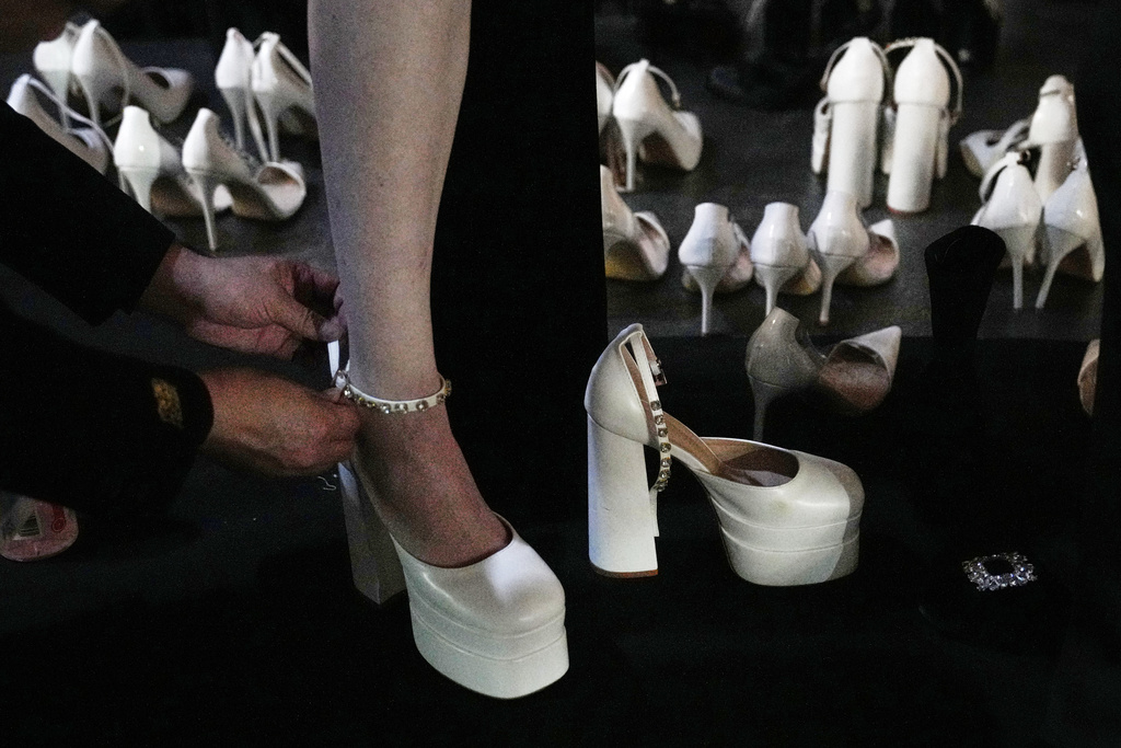 An assistant helps a model wearing a shoes at backstage as they preparing to showcase a creations by Xiong Ying - Heaven Gala during China Fashion Week 2026, in Beijing, China, Friday, March 20, 2026. (AP Photo/Andy Wong)