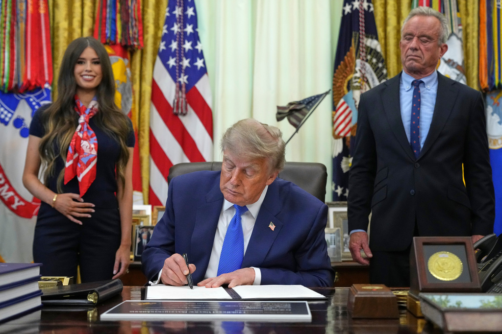 President Donald Trump signs an executive order about vaccines as Jayme Franklin, left, and Health and Human Services Secretary Robert F. Kennedy Jr. watch Monday, Aug. 10, 2026, in the Oval Office of the White House in Washington. (AP Photo/Jacquelyn Martin)
