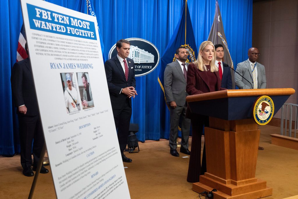 Attorney General Pam Bondi stands near wanted poster for Canadian fugitive Ryan James Wedding as she speaks with reporters during a news conference at the Department of Justice, Wednesday, Nov. 19, 2025, in Washington. (AP Photo/Mark Schiefelbein)