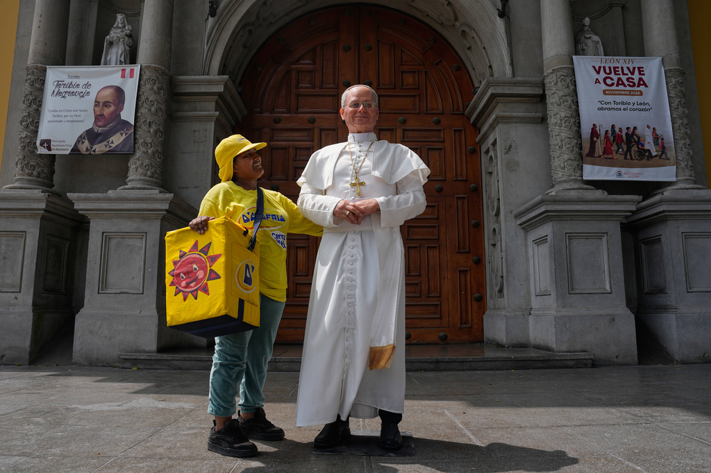Ice cream vendor Alicia Caso touches a life-size statue of Pope Leo XIV standing on display outside a church in the Barranco neighborhood of Lima, Peru, Tuesday, Oct. 13, 2026, a month before the pope's visit to Peru. (AP Photo/Martin Mejia)