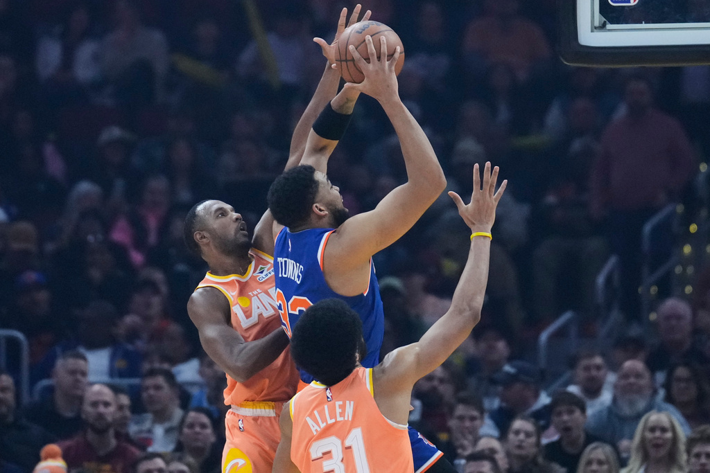 New York Knicks center Karl-Anthony Towns (32) shoots between Cleveland Cavaliers center Evan Mobley, left, and center Jarrett Allen (31) in the first half of an NBA basketball game in Cleveland, Tuesday, Feb. 24, 2026. (AP Photo/Sue Ogrocki)