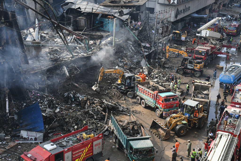 Rescue workers and firefighters work with heavy machinery to search through the rubble of a burnt building of a multistory shopping plaza following a massive fire in Karachi, Pakistan, Monday, Jan. 19, 2026. (AP Photo/Ali Raza)