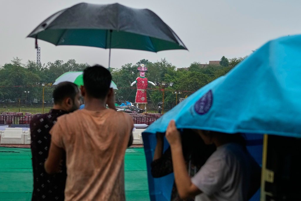 Organizers shelter under umbrellas and plastic sheeting as a sudden rain and thunderstorm causes the effigy of demon king Ravan and others to fall and sustain water damage during the Hindu festival of Dussehra in New Delhi, India, Thursday, Oct. 2, 2025. (AP Photo/Manish Swarup)