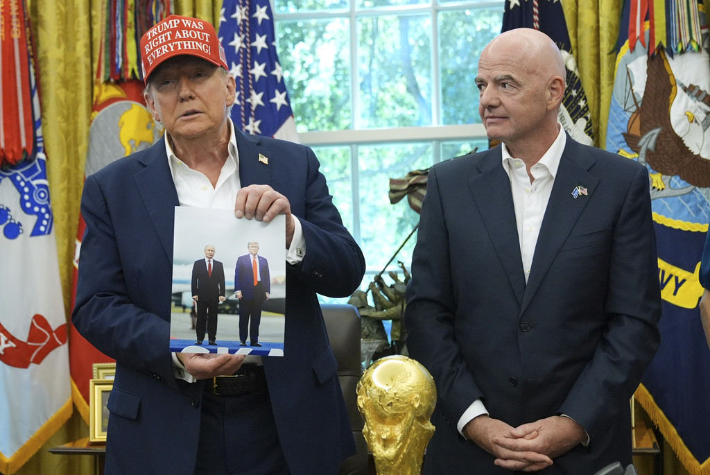 President Donald Trump holds a photo of himself with Russian President Vladimir Putin as FIFA President Gianni Infantino watches during an announcement in the Oval Office of the White House, Friday, Aug. 22, 2025, in Washington. (AP Photo/Jacquelyn Martin)