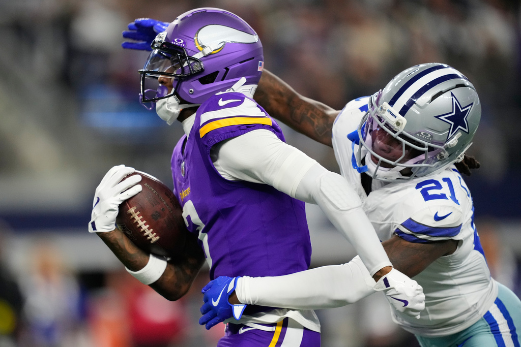 Minnesota Vikings wide receiver Jordan Addison, left, runs with the ball as Dallas Cowboys cornerback Caelen Carson defends during the first half of an NFL football game Sunday, Dec. 14, 2025, in Arlington, Texas. (AP Photo/Tony Gutierrez)