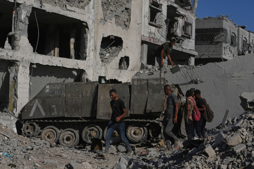 Palestinians inspect a damaged armored personnel carrier left behind by Israeli forces amid destroyed buildings in the Zeitoun neighborhood of Gaza City, Friday, Oct. 10, 2025, after Israel and Hamas agreed to pause their war and release the remaining hostages. (AP Photo/Jehad Alshrafi)