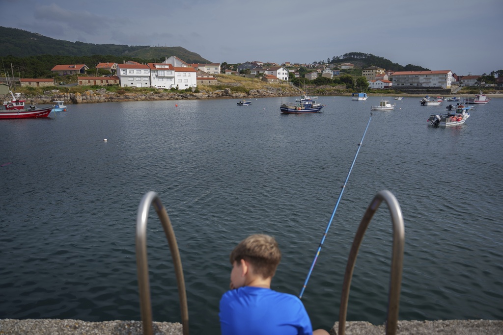 A young boy waits to catch a fish Tuesday, June 24, 2025, in Lira, Spain. (AP Photo/Annika Hammerschlag).