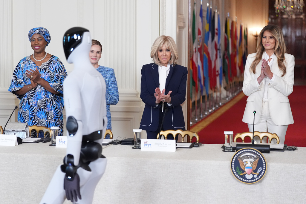 First lady Melania Trump arrives, accompanied by a robot, to attend the "Fostering the Future Together Global Coalition Summit," with other first spouses, at the White House, Wednesday, March 25, 2026, in Washington. From left are Dr. Fatima Maada Bio, of Sierra Leone, Martha Nawrocka of Poland, Brigitte Macron of France and Melania Trump. (AP Photo/Jacquelyn Martin)