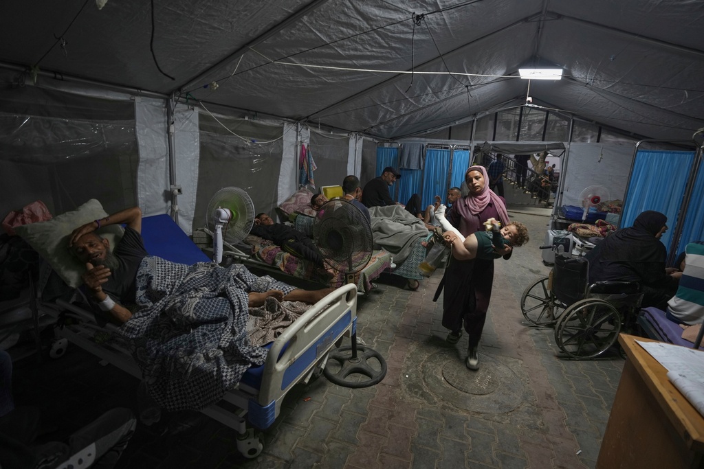 A mother carries her child into a patient treatment tent set up in the yard of Shifa Hospital in Gaza City, Friday, July 4, 2025. (AP Photo/Jehad Alshrafi)