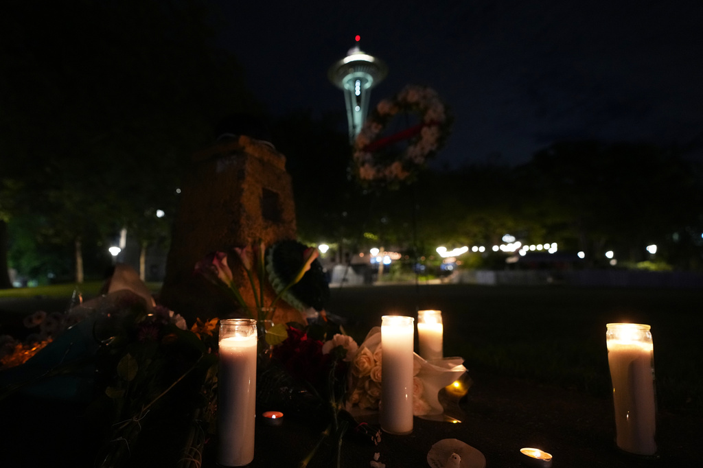 Flowers and candles are seen placed with the Space Needle at background, during the vigil for victims the day after a shooting at Seattle Center during the Bite of Seattle food festival, Monday, July 27, 2026, in Seattle. (AP Photo/Lindsey Wasson)