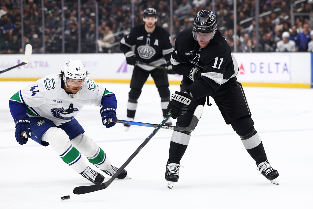 Los Angeles Kings center Anze Kopitar (11) passes the puck against Vancouver Canucks left wing Kiefer Sherwood (44) as Los Angeles Kings right wing Adrian Kempe, back center, watches during the second period of an NHL hockey game, Saturday, Nov. 29, 2025, in Los Angeles. (AP Photo/Jessie Alcheh)