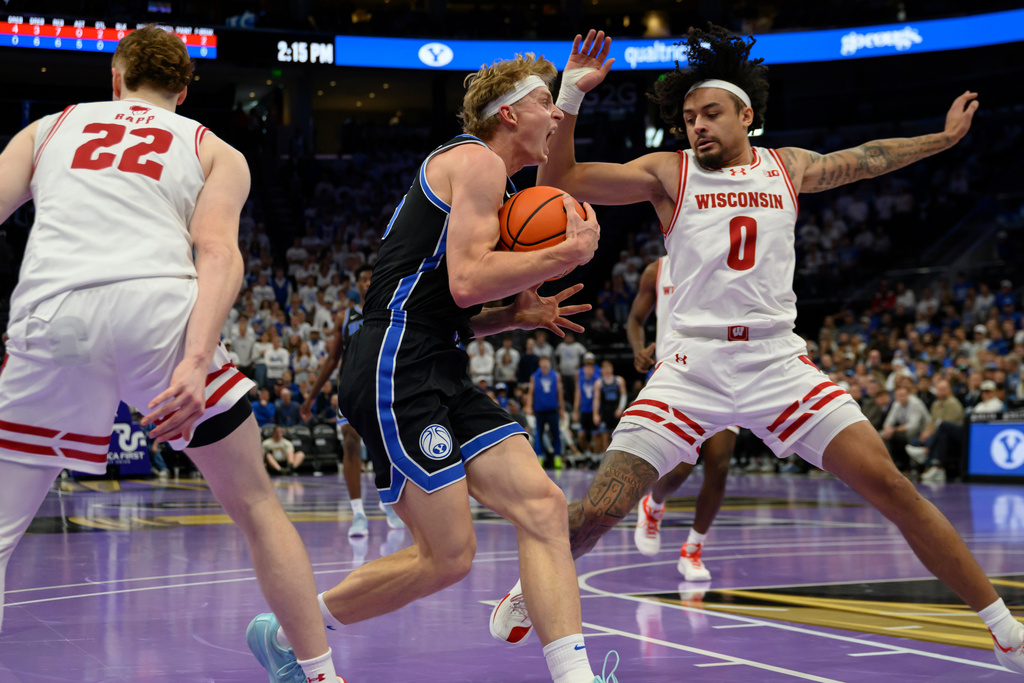 BYU guard Richie Saunders, center, is fouled by Wisconsin guard Braeden Carrington (0) as he drives to the basket during the first half of an NCAA college basketball game, Friday, Nov. 21, 2025, in Salt Lake City. (AP Photo/Tyler Tate)