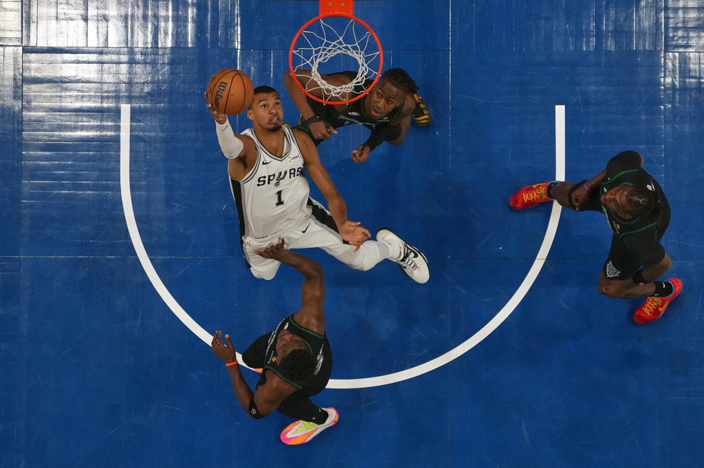 San Antonio Spurs forward Victor Wembanyama, middle, shoots over Minnesota Timberwolves guards Ayo Dosunmu (13), top, and Anthony Edwards (5), bottom, during the first half of Game 6 of a NBA basketball second-round playoff series, Friday, May 15, 2026, in Minneapolis. (AP Photo/Abbie Parr)