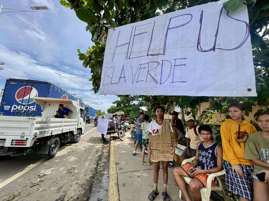 Residents of Isla Verde stand beside a sign which they made to call for help as they return to their damaged homes after Typhoon Kalmaegi caused devastation in communities along the Mananga River in Talisay City, Cebu province, central Philippines, Wednesday, Nov. 5, 2025. (AP Photo/Jacqueline Hernandez)
