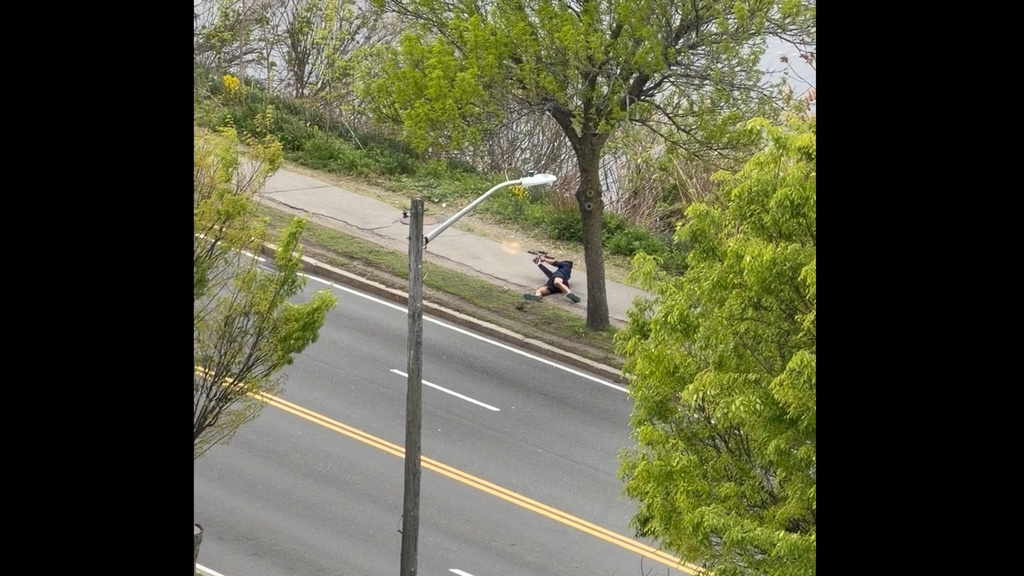 This image taken from video provided by Youssef Adel, shows a man with an assault-style rifle firing his weapon at a busy road outside at in Cambridge, Mass. on Monday, May 11, 2026. (Youssef Adel via AP)